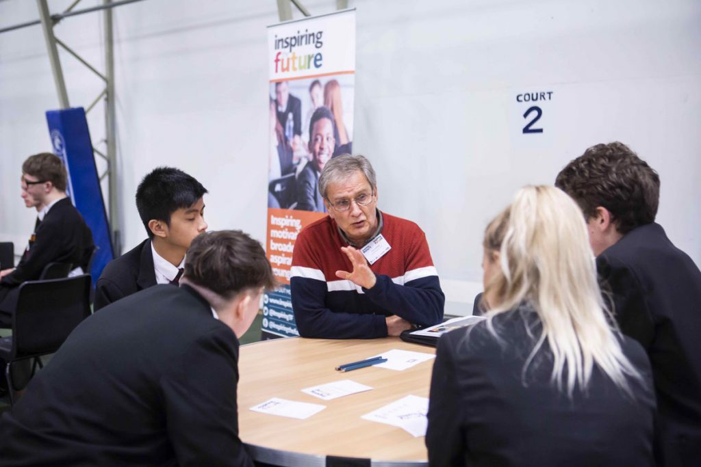 A man talking to four students sat at a table 